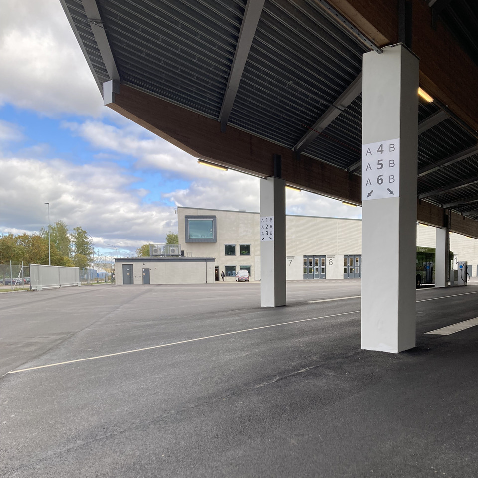 Bild på Växjö stadsbussdepå med kontors- och verkstadsbyggnad. Byggnaden har vågformade betongelement, återbrukat tegel, grönt tak och solceller – vilket visar på både estetisk omsorg och hållbarhet.